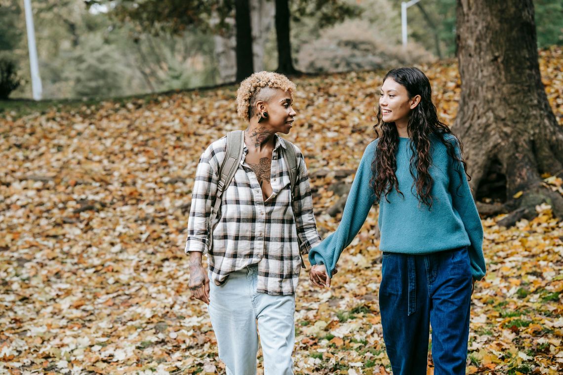 two women holding hands walking in a park